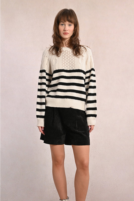 Person wearing a black and white striped sweater with black shorts on a plain background