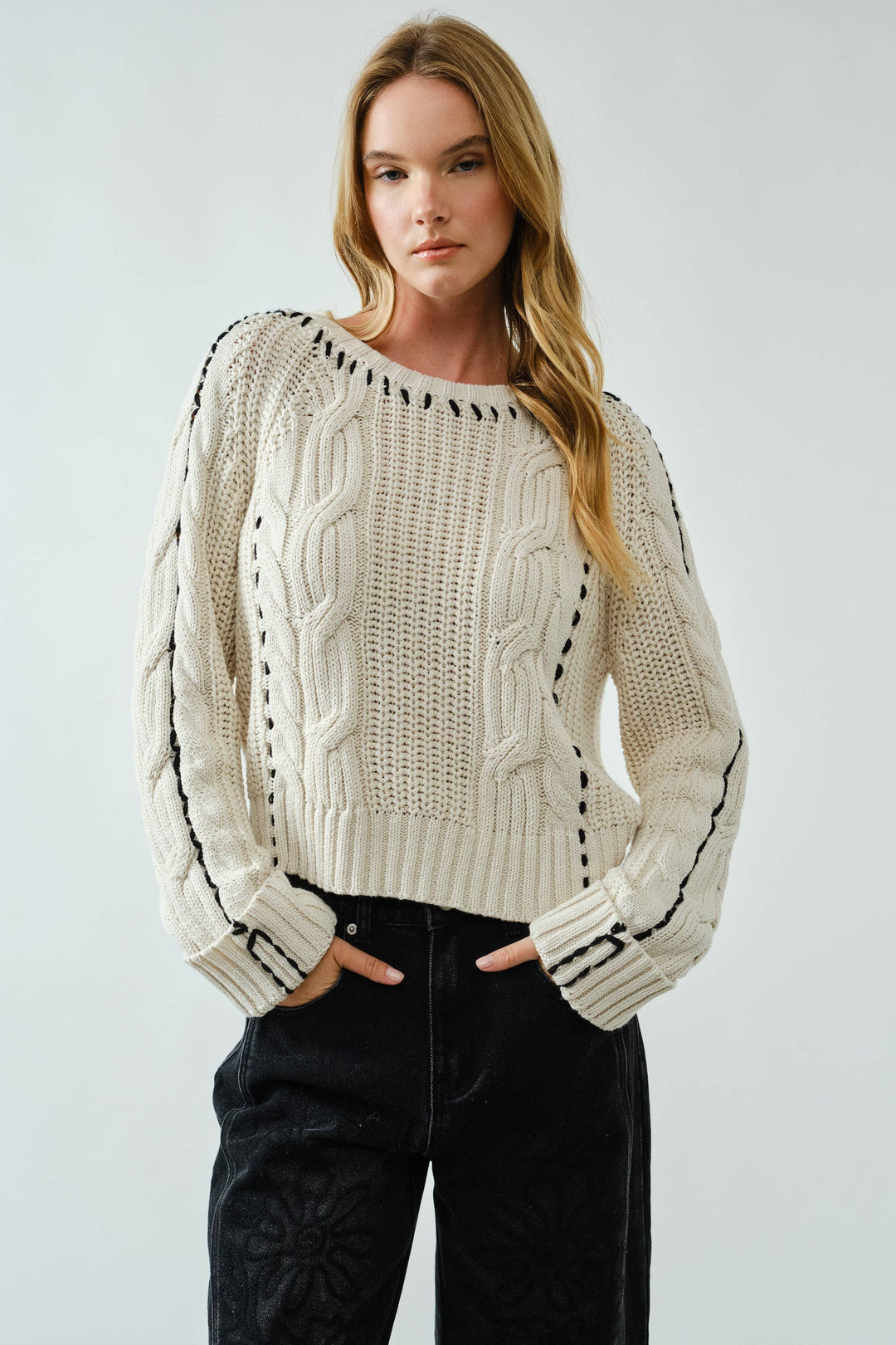 Woman wearing a cream sweater with black accents on a plain background