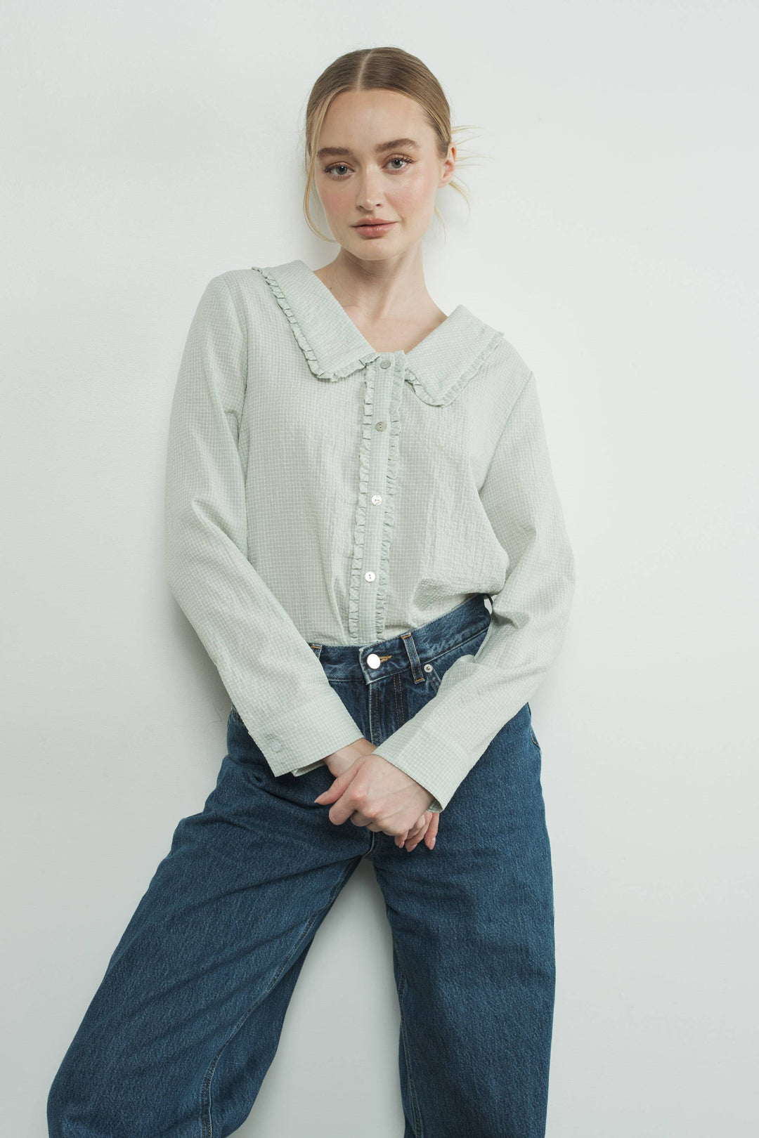 Woman wearing a light-colored blouse with a collar and blue jeans on a white background