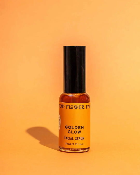 Bottle of 'Golden Glow' facial serum from 'Good Flower Farm' on an orange background
