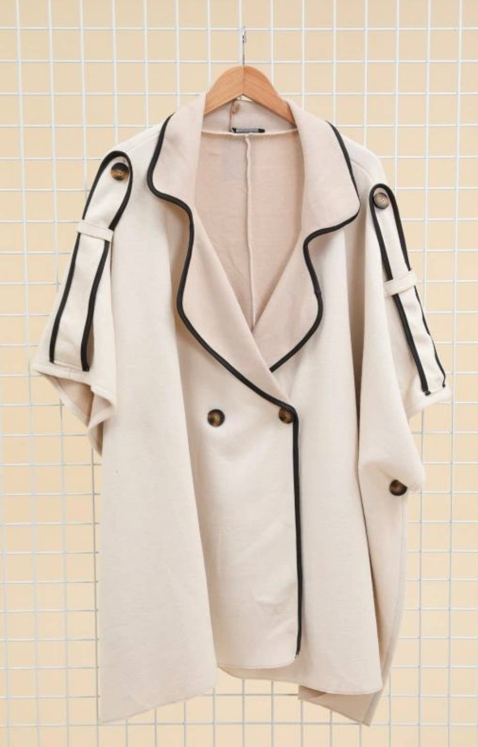White coat with black trim on a hanger against a tiled wall background