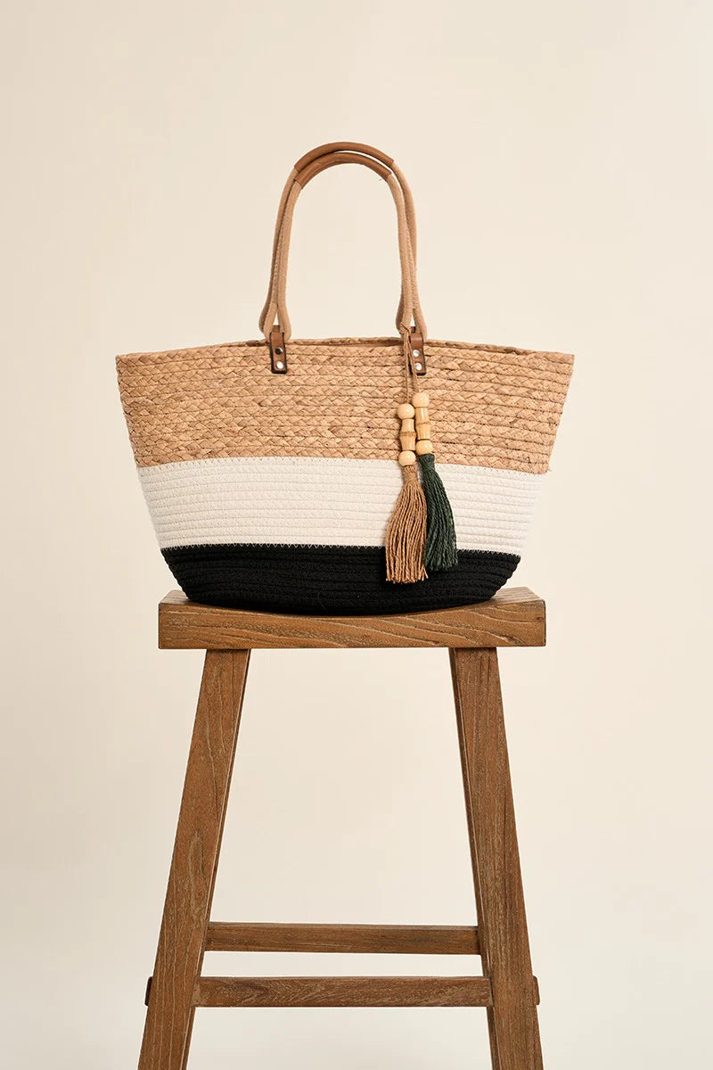 Woven tote bag with a tassel on a wooden stool against a beige background