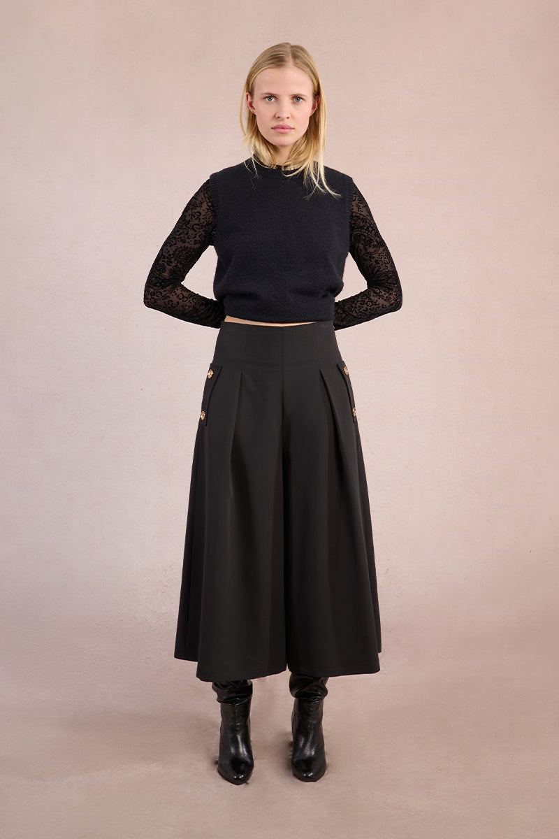 Woman wearing a black outfit with sheer sleeves against a beige background