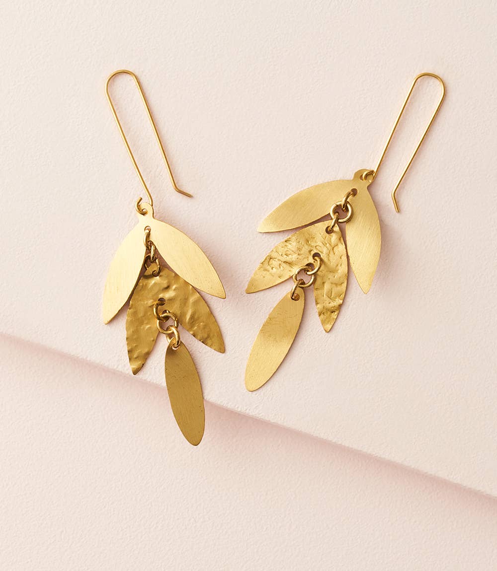 Gold leaf-shaped earrings on a light pink background