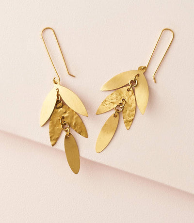 Gold leaf-shaped earrings on a light pink background