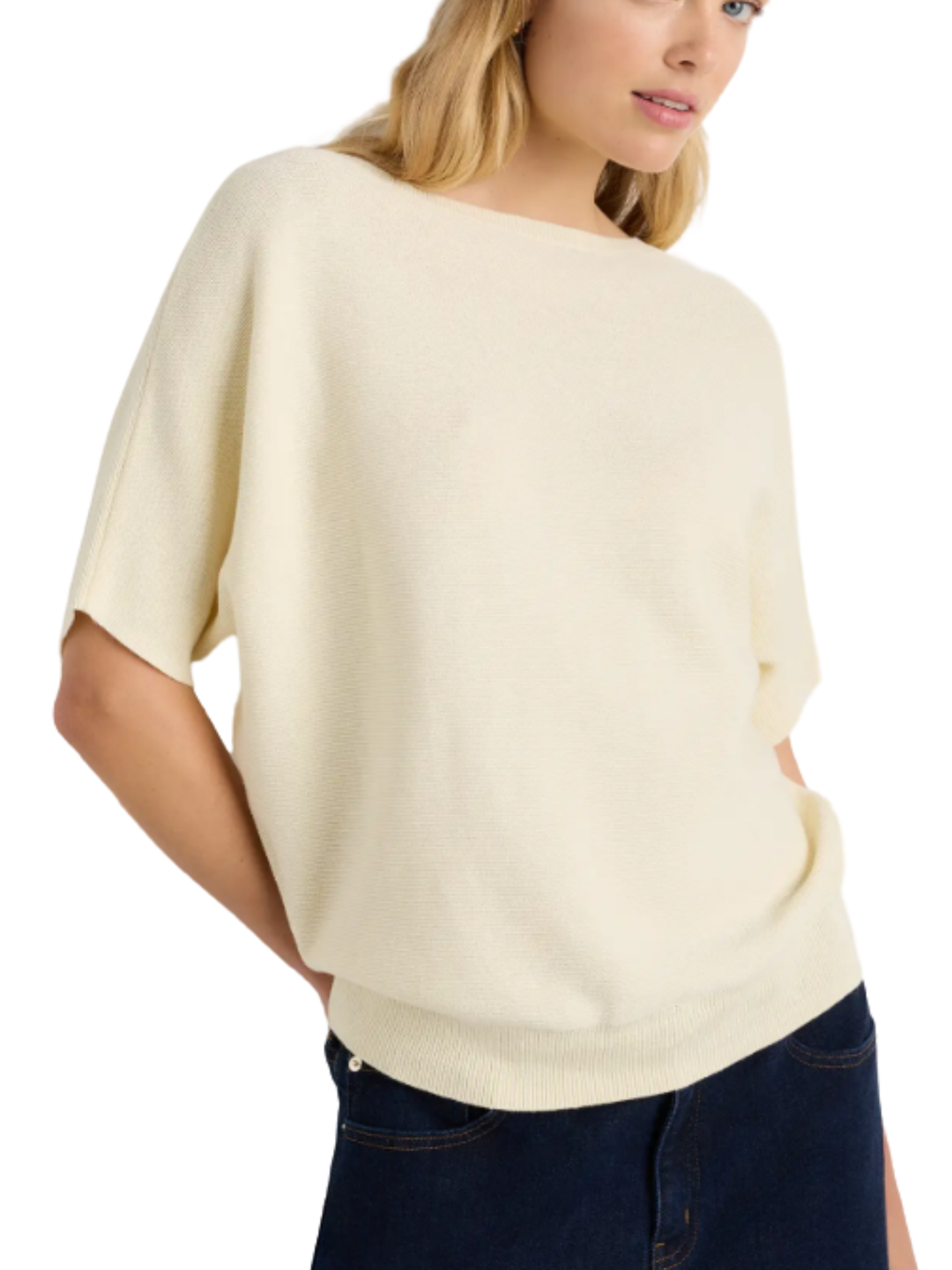 Woman wearing a beige sweater and dark jeans on a white background