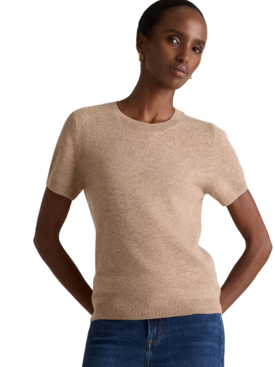 Woman wearing a beige sweater and blue jeans on a white background