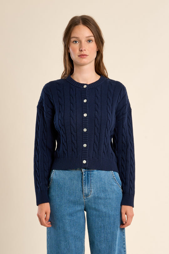 Woman wearing a navy blue cable knit cardigan with white buttons on a beige background
