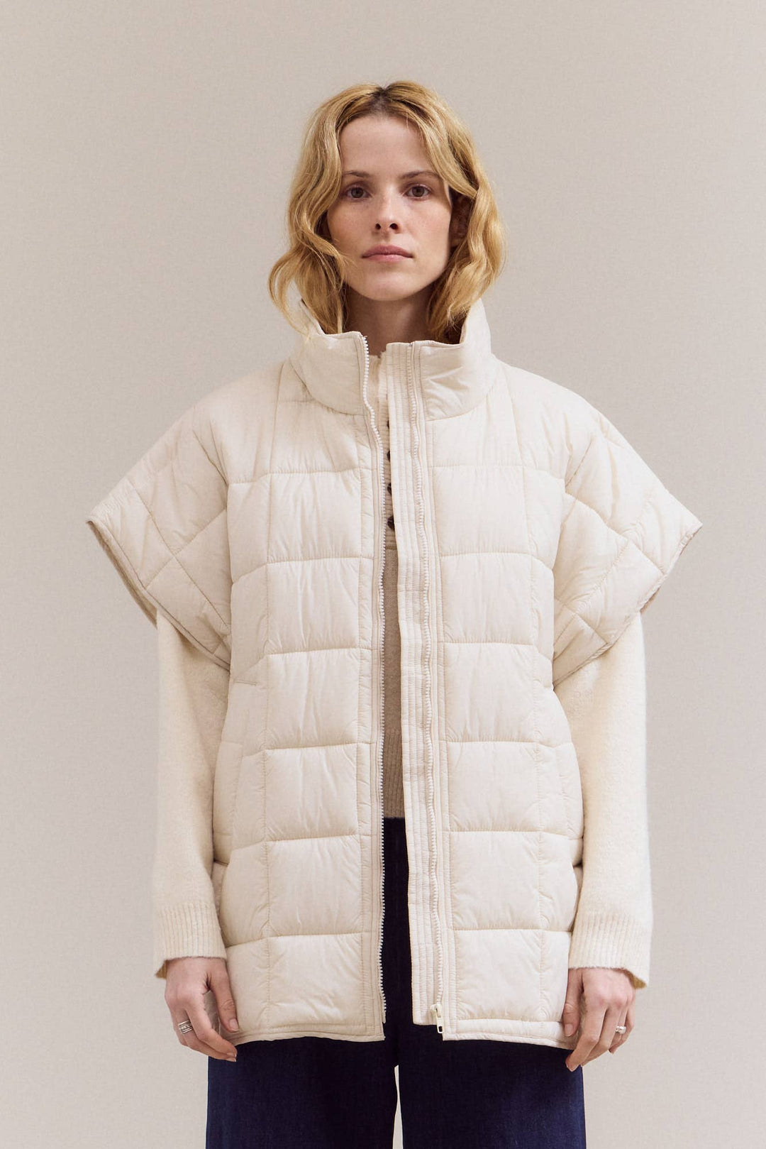 Woman wearing a beige puffer jacket against a plain background