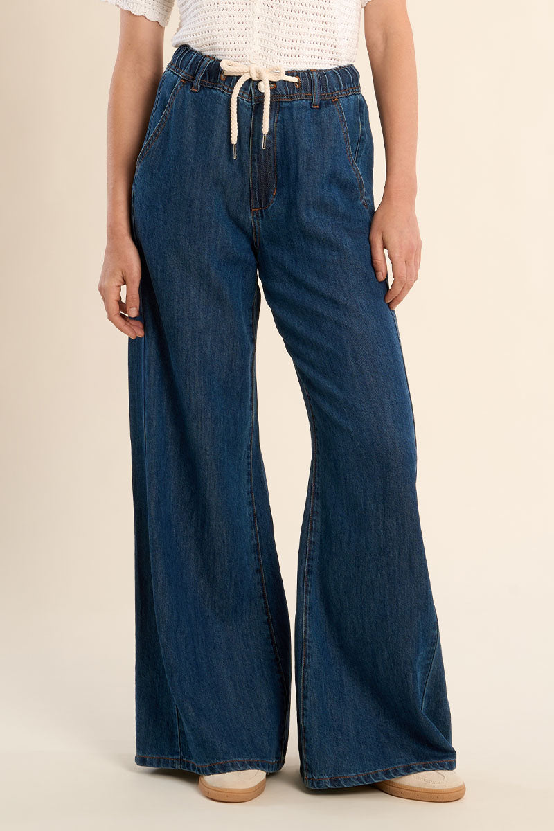 Person wearing blue wide-leg jeans on a beige background