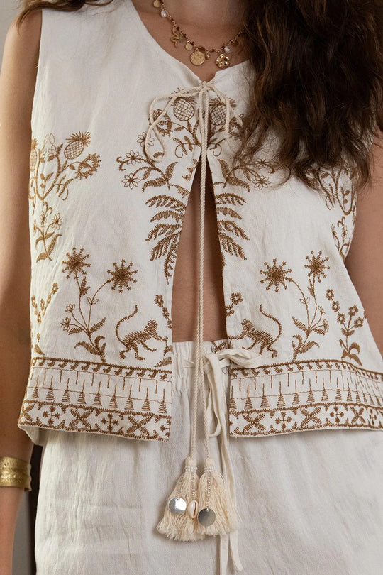 White sleeveless top with intricate gold embroidery on a person wearing it.