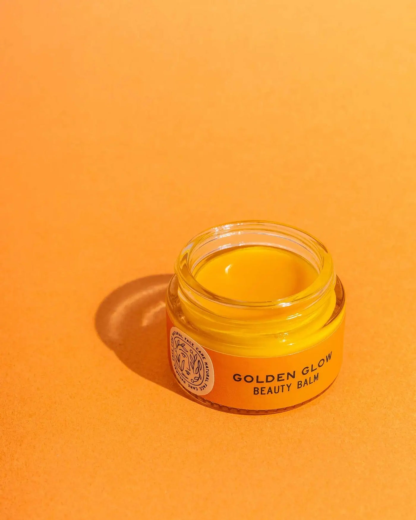 Jar of 'Golden Glow Beauty Balm' on an orange background