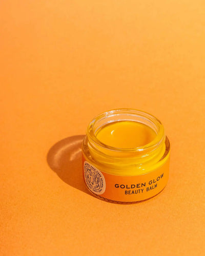Jar of 'Golden Glow Beauty Balm' on an orange background