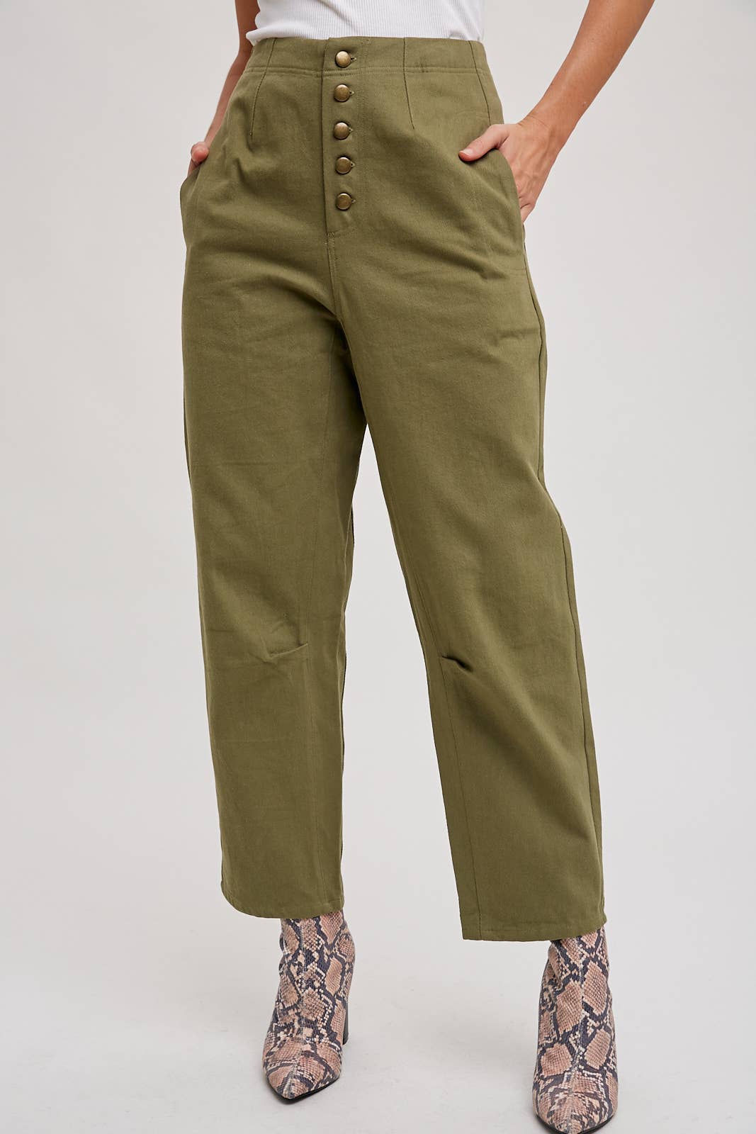 Person wearing olive green pants with button details on a white background