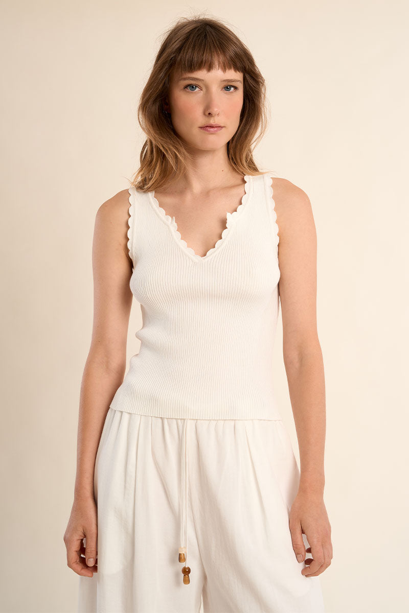 Woman wearing a white sleeveless top and pants against a beige background
