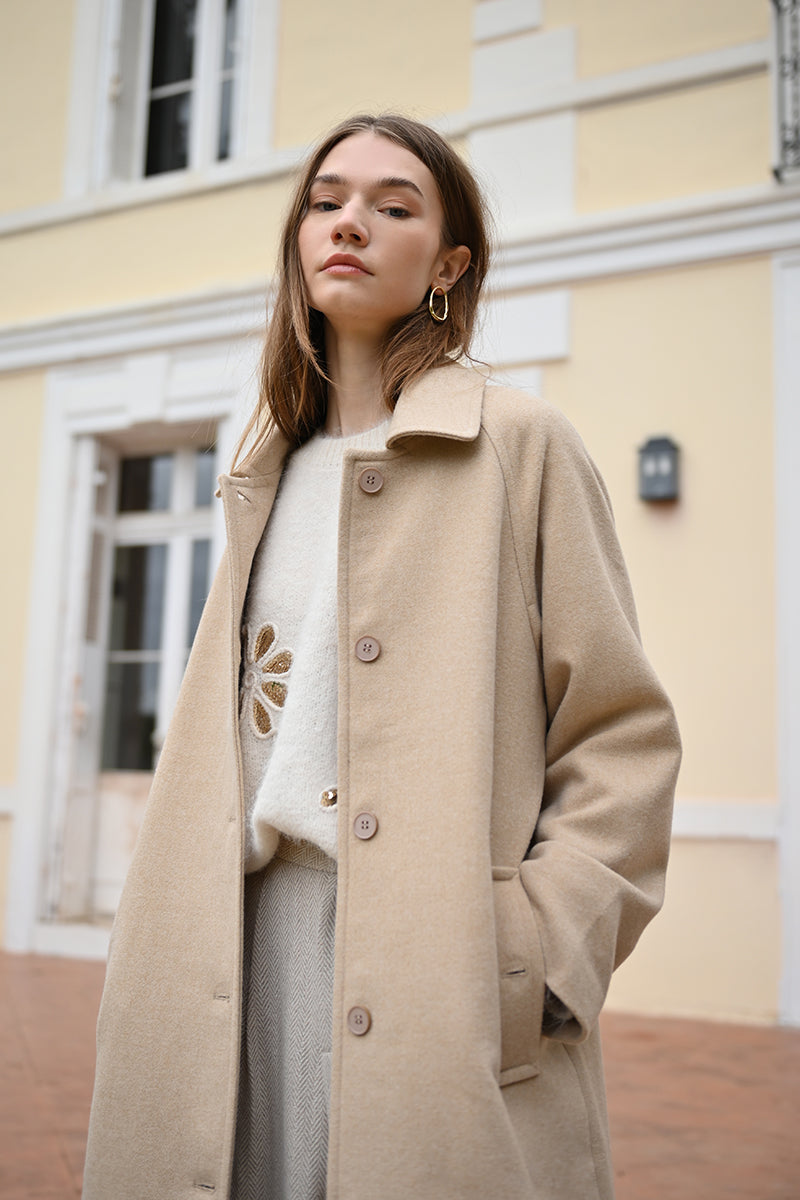 Woman wearing a beige coat standing in front of a building