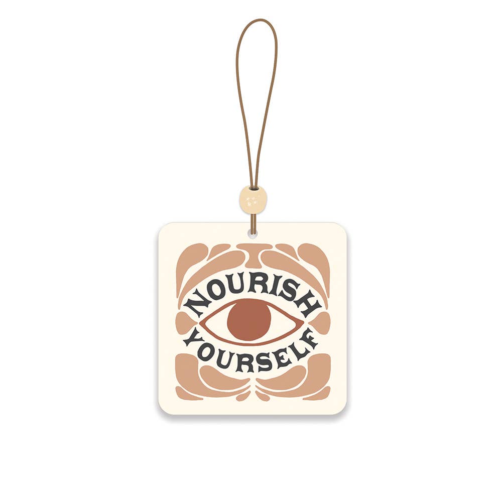 Decorative car freshener with 'Nourish Yourself' text and an eye design on a beige background.