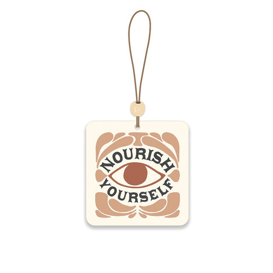 Decorative car freshener with 'Nourish Yourself' text and an eye design on a beige background.