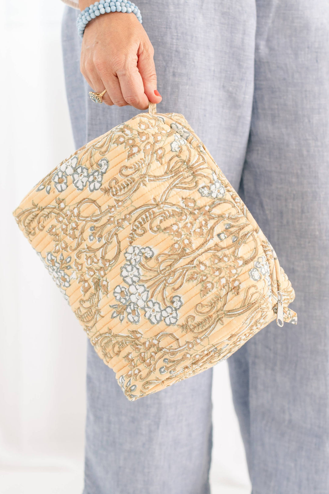 Beige clutch bag with floral embroidery held by a person wearing light blue pants against a white background