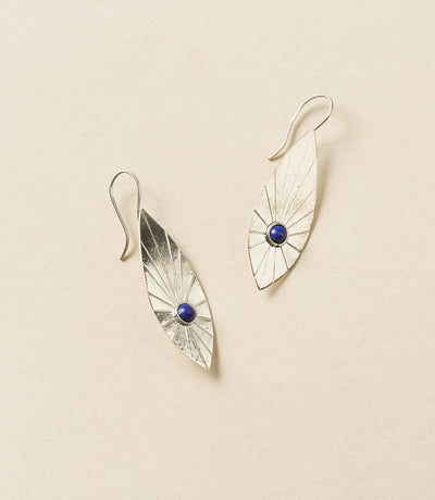 Pair of silver earrings with blue gemstones on a beige background