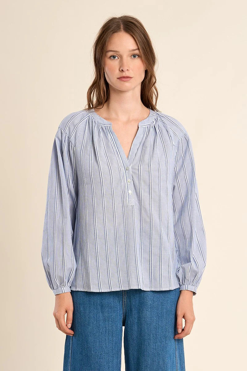 Woman wearing a blue and white striped blouse with blue jeans on a beige background