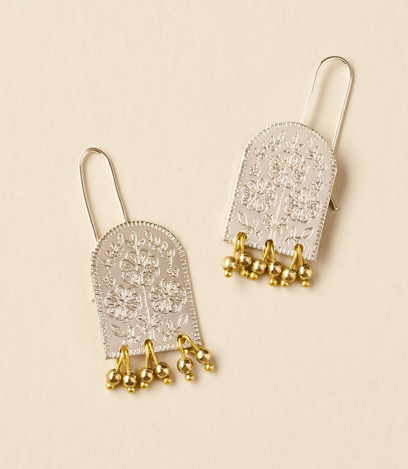 Pair of silver and gold earrings on a beige background