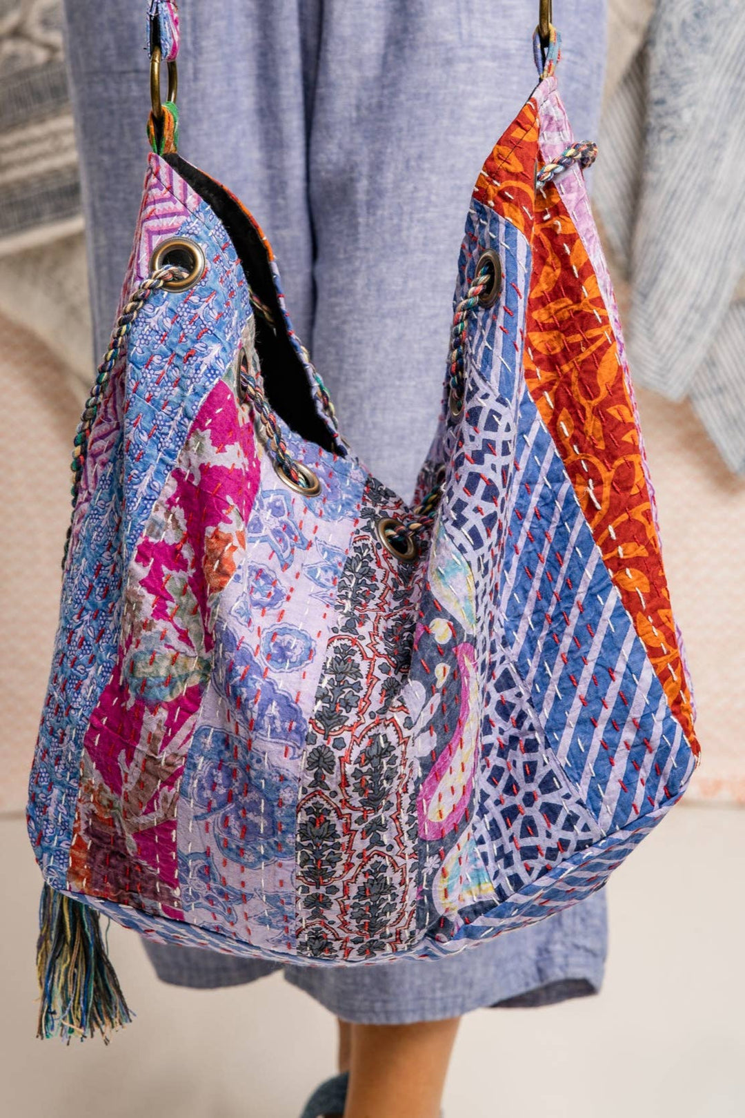 Colorful patterned bag with tassels held by a person wearing a blue dress.