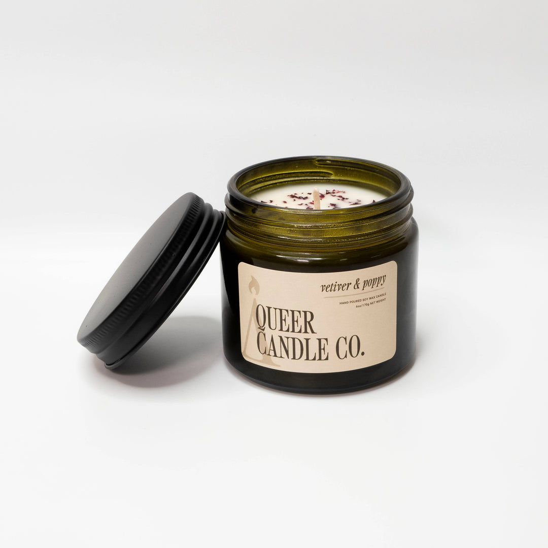 Green candle jar with lid open, displaying 'Queer Candle Co.' label on a white background