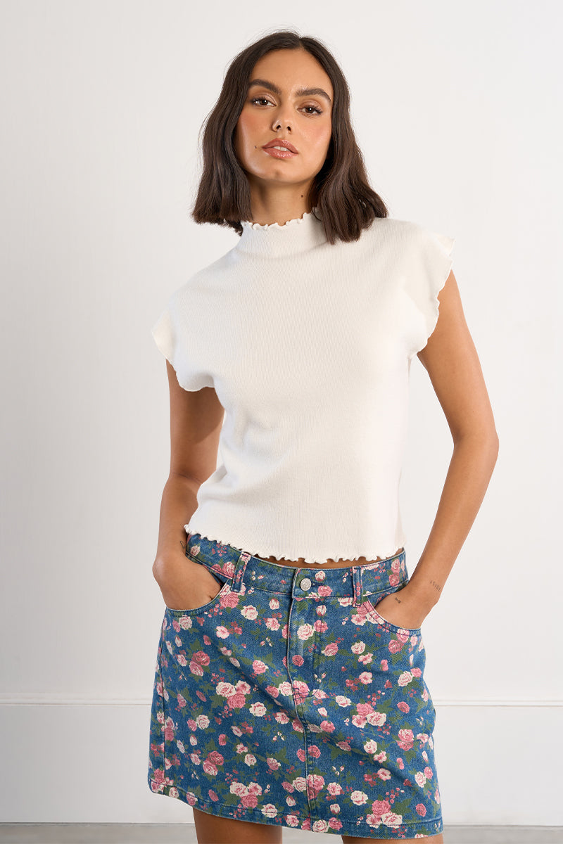 Woman wearing a white top and floral skirt against a plain background
