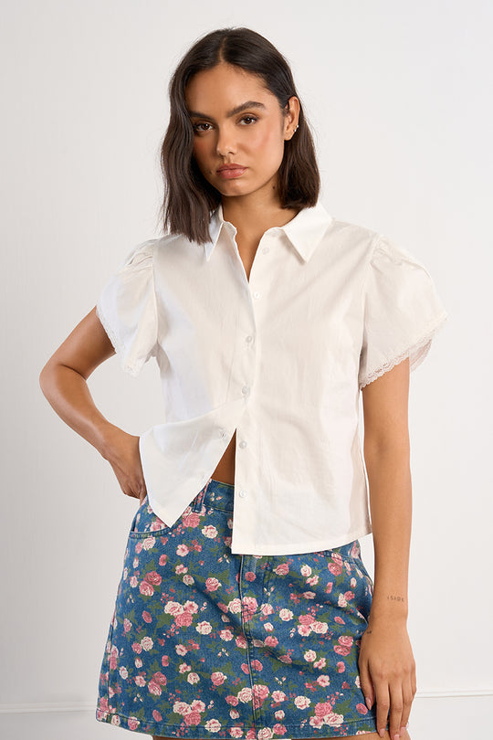 Woman wearing a white blouse and floral skirt on a plain background