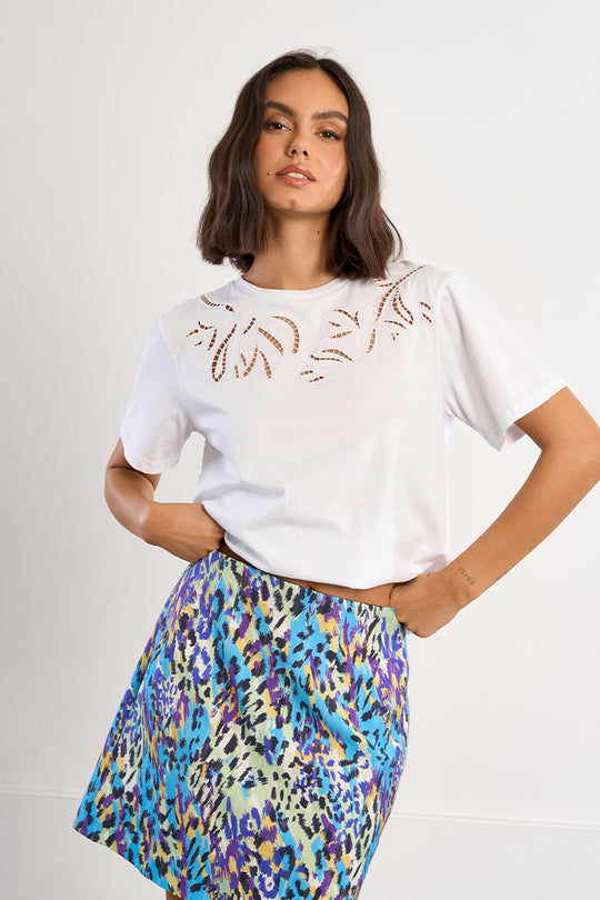 Woman wearing a white t-shirt with cut-out designs and a colorful patterned skirt on a plain background